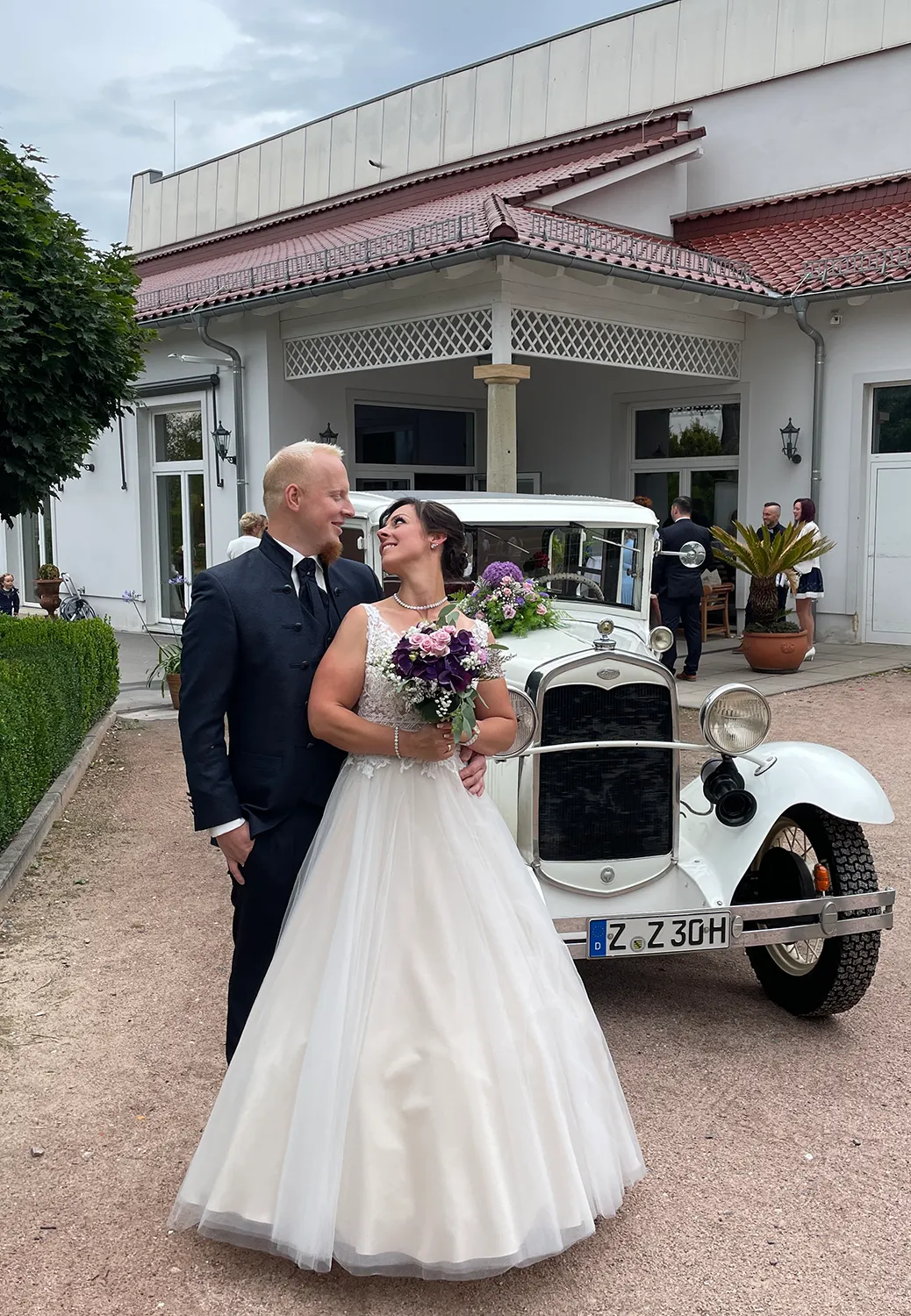 Glückliches Brautpaar mit Oldtimer vor Hochzeitslocation – romantischer Hochzeitstag mit DJ Dobbi als musikalischer Begleitung